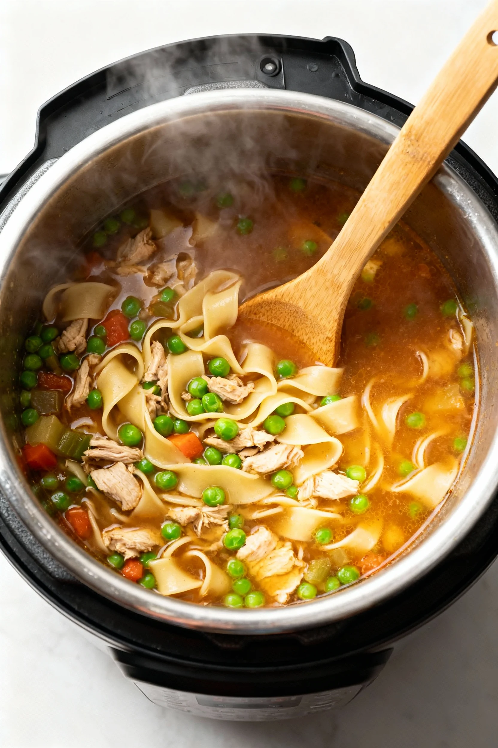 Overhead shot of Instant Pot turkey noodle soup after simmering: tender noodles and bright green peas in deglazed rich b