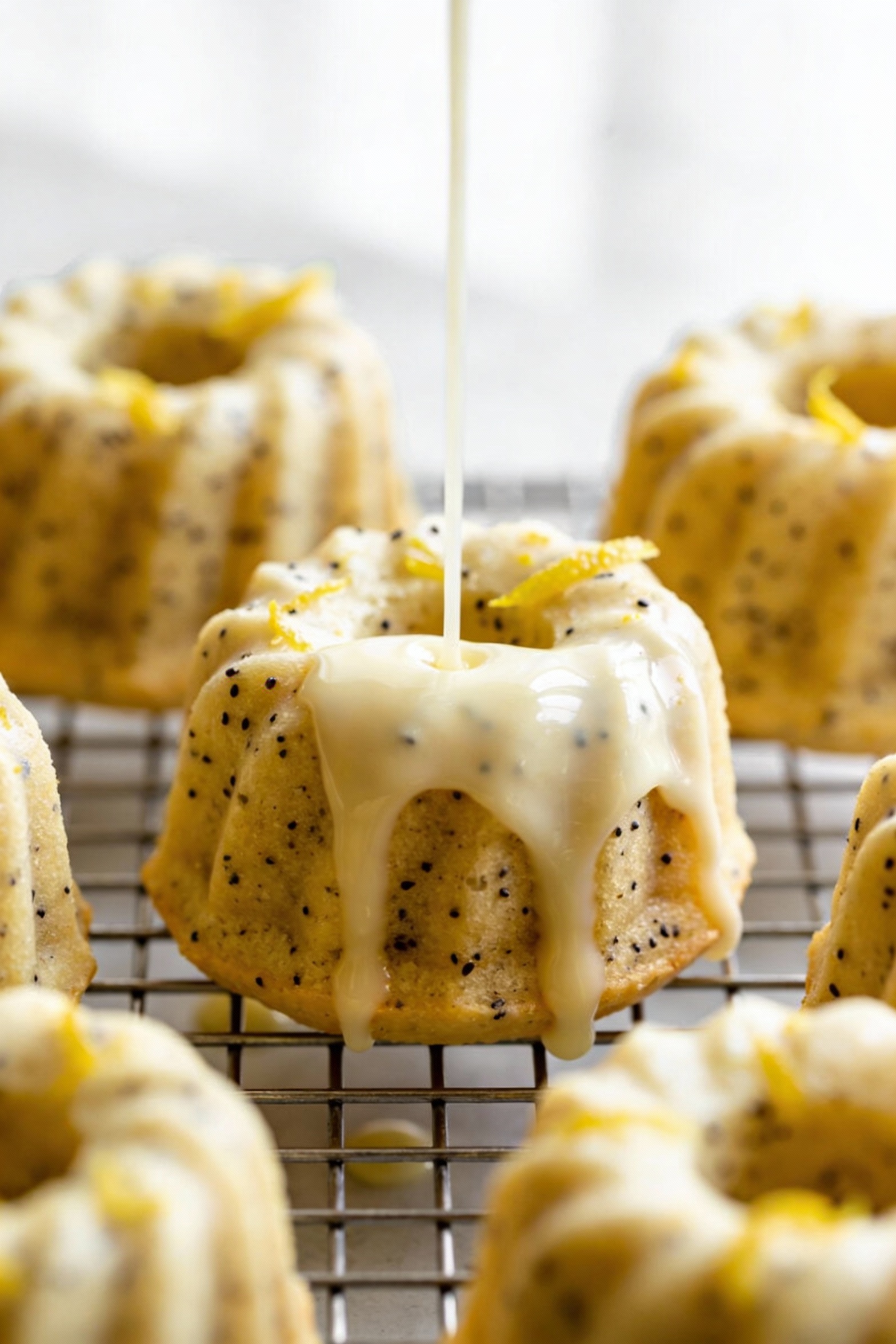 Close-up detail of a glossy lemon glaze dripping into the deep ridges of mini lemon poppy seed bundt cakes, visible popp