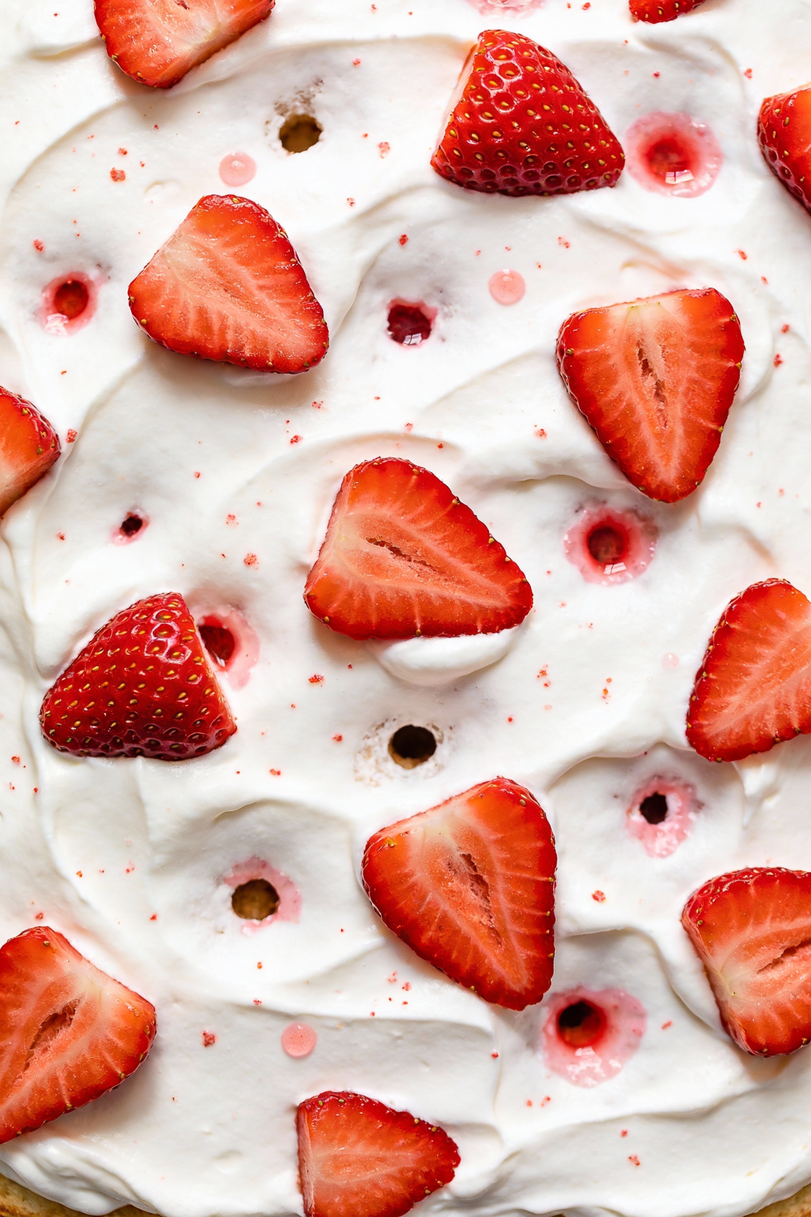 Overhead shot of strawberries-and-cream poke cake: white cake fully topped with a smooth whipped topping layer, scattere