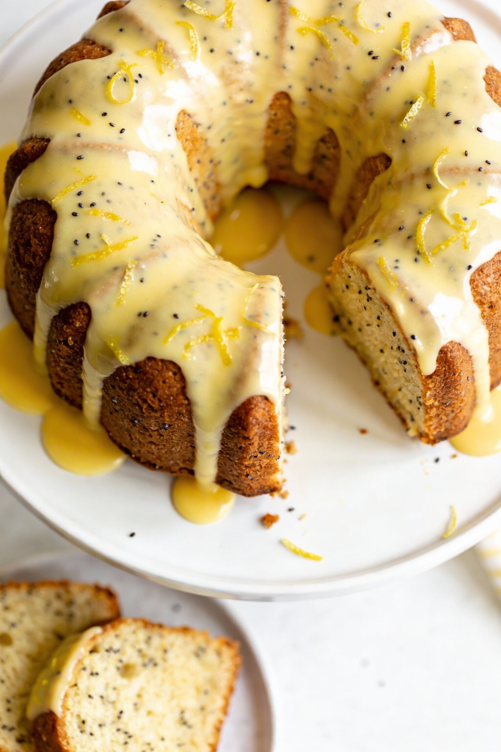 Overhead shot of a lemon poppy seed bundt cake on a white cake stand, lemon glaze poured as a smooth glossy curtain, vis