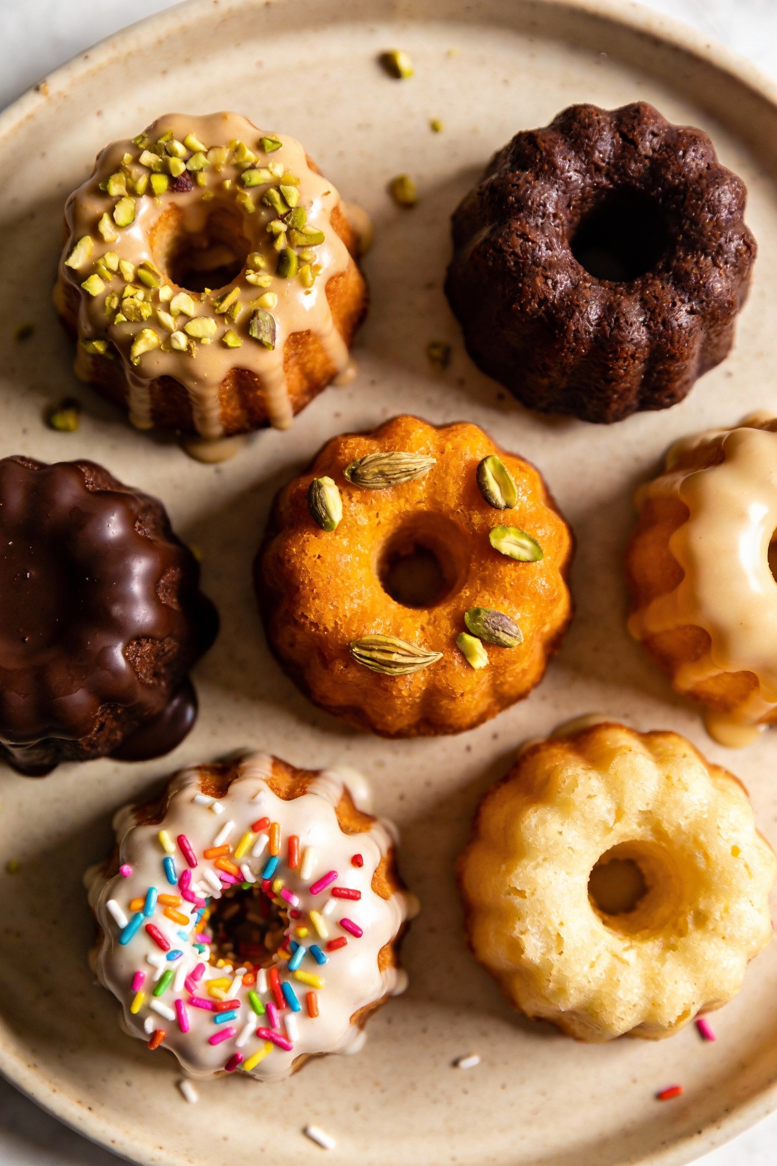Overhead shot of assorted finished mini bundt cakes (chocolate espresso, orange cardamom with chopped pistachios, confet