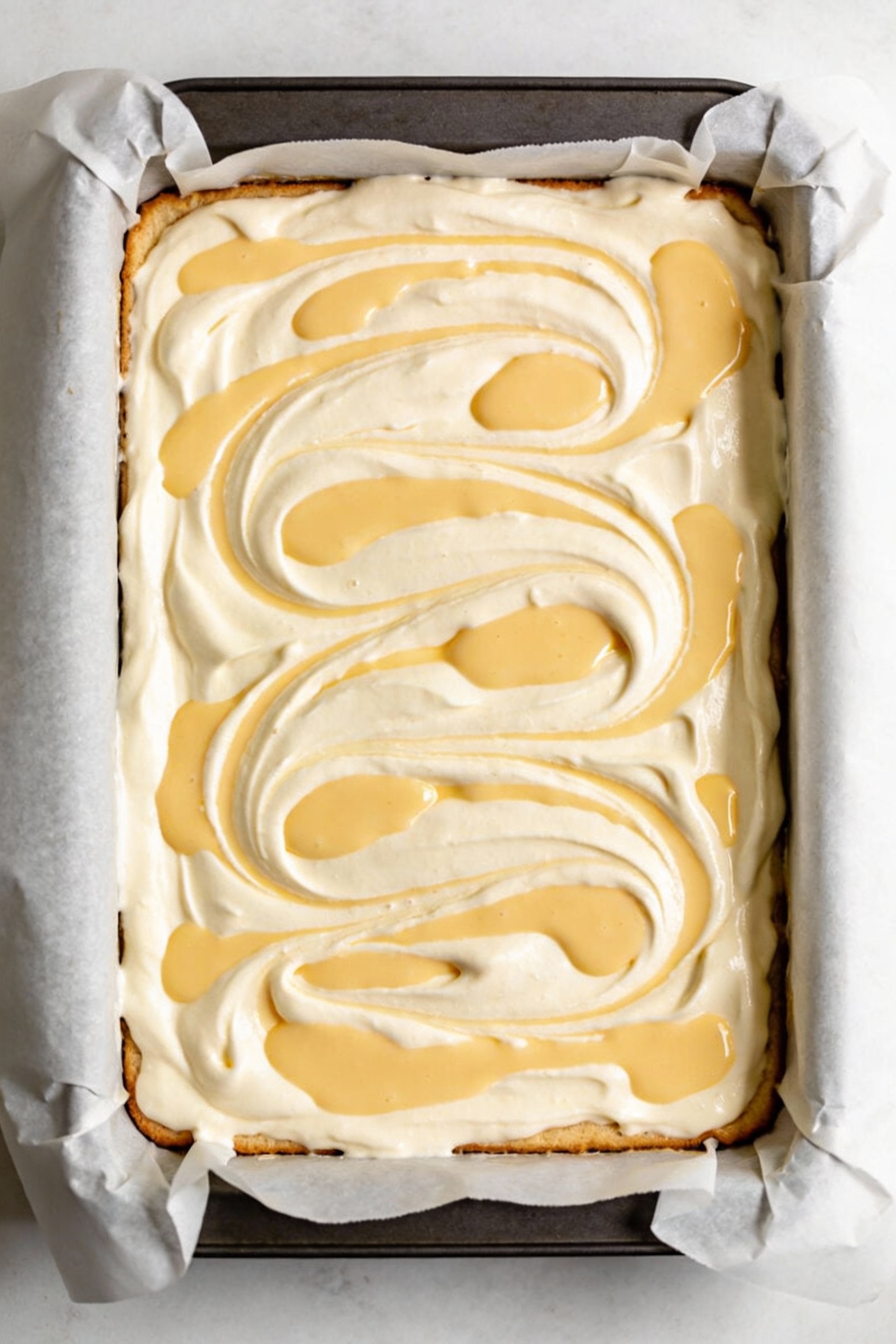 2. Overhead shot of a 9x13 custard swirl sheet cake right before baking, dollops of pale-yellow custard marbled into smo