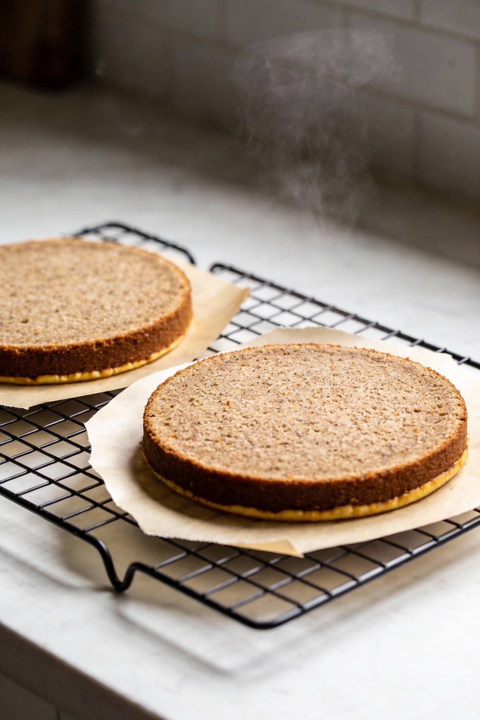 3. Cooking process: two baked gluten-free cake layers cooling on a wire rack with parchment rounds peeled back slightly,