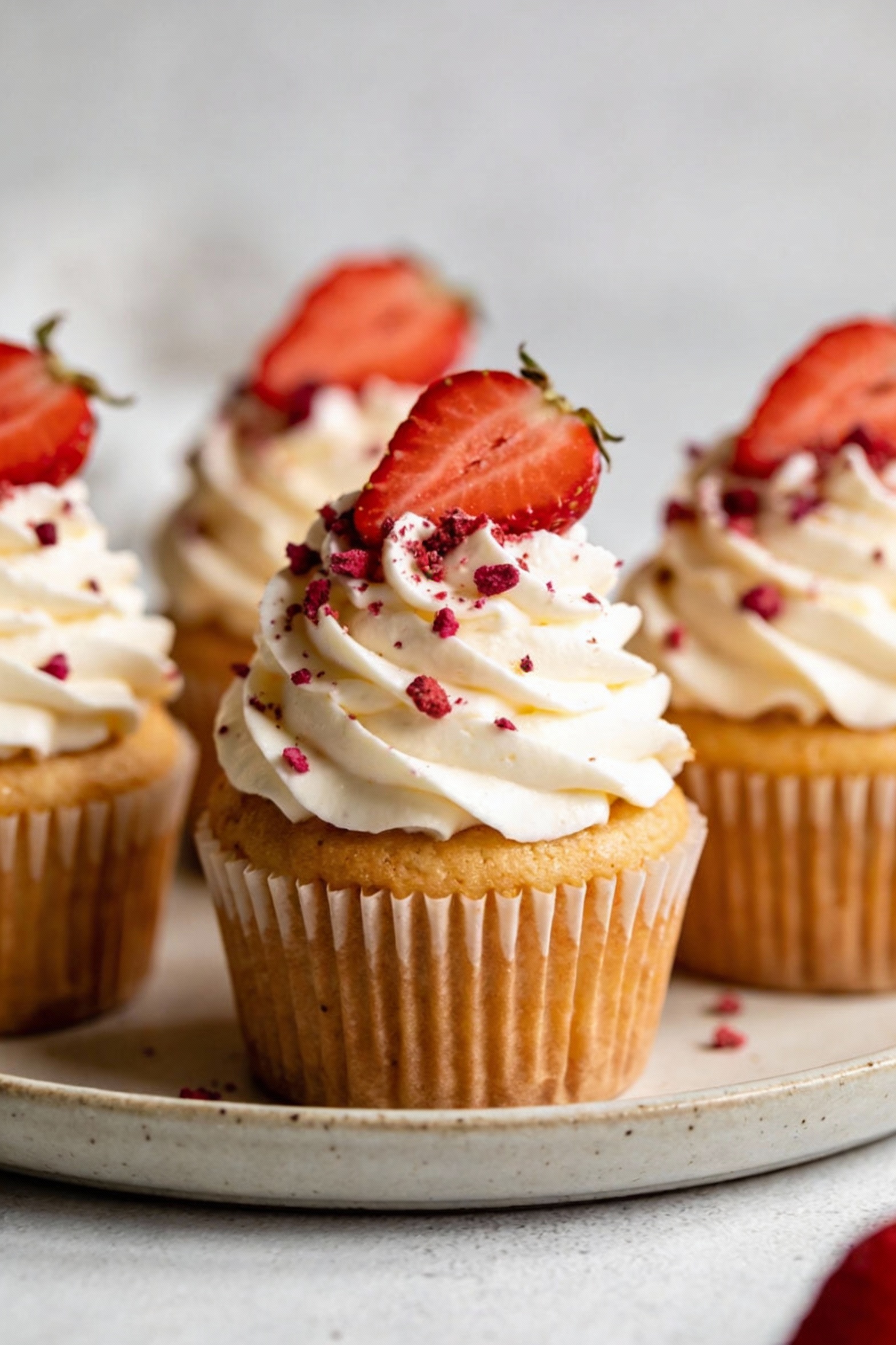3. Strawberry cupcakes with cream cheese frosting piped in tall swirls, topped with a fresh strawberry slice and a sprin