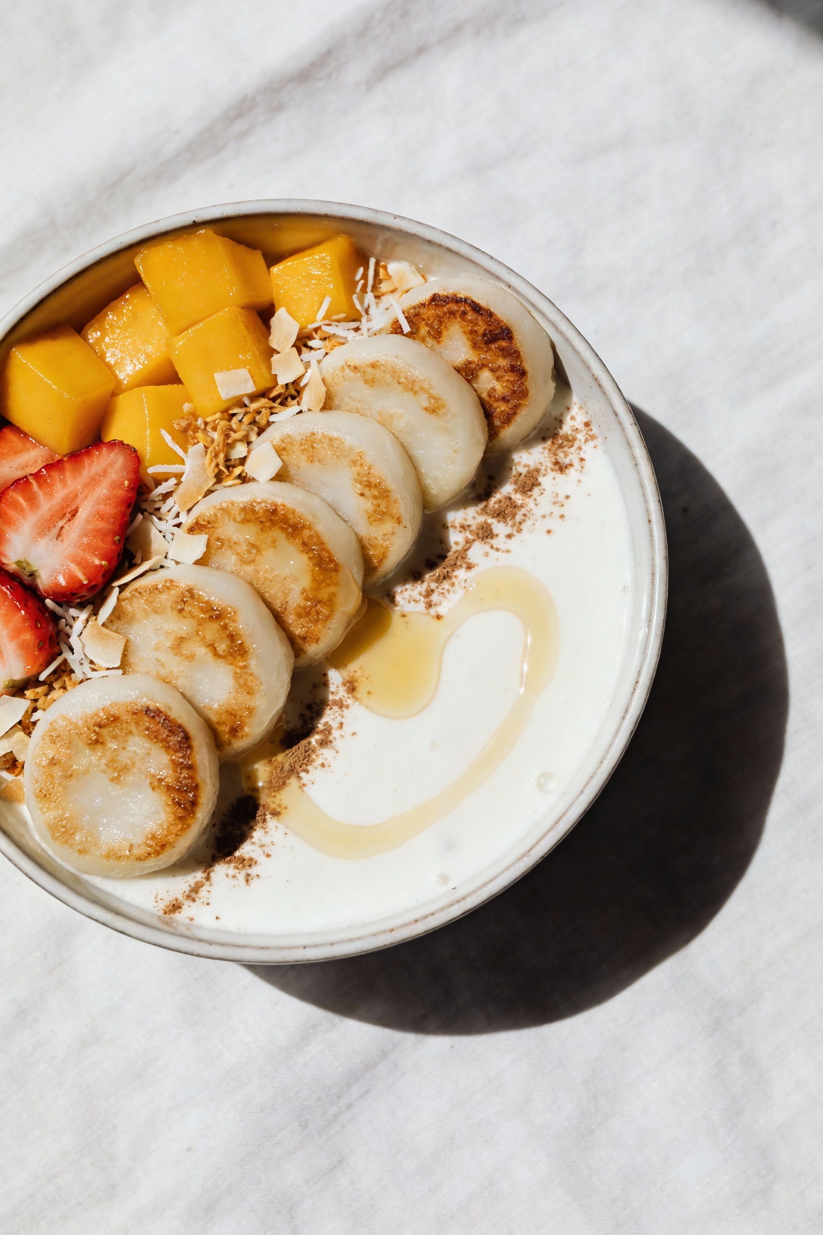 Top-view dessert bowl: sweet coconut rice cake bowl with silky coconut milk base, sliced pan-seared mochi/rice cakes, ma