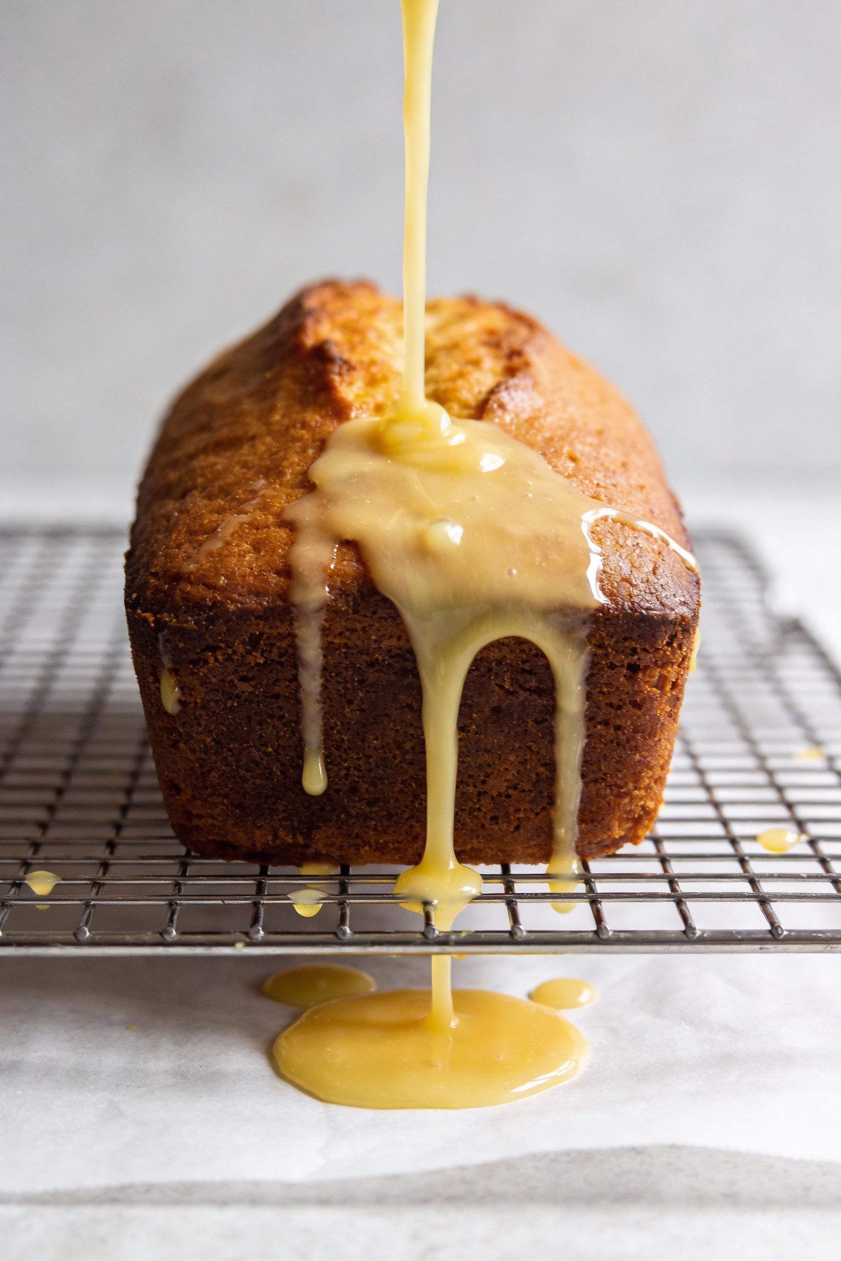 Cooking process: warm loaf on a cooling rack being glazed; a stream of pourable lemon glaze cascading over the barely wa