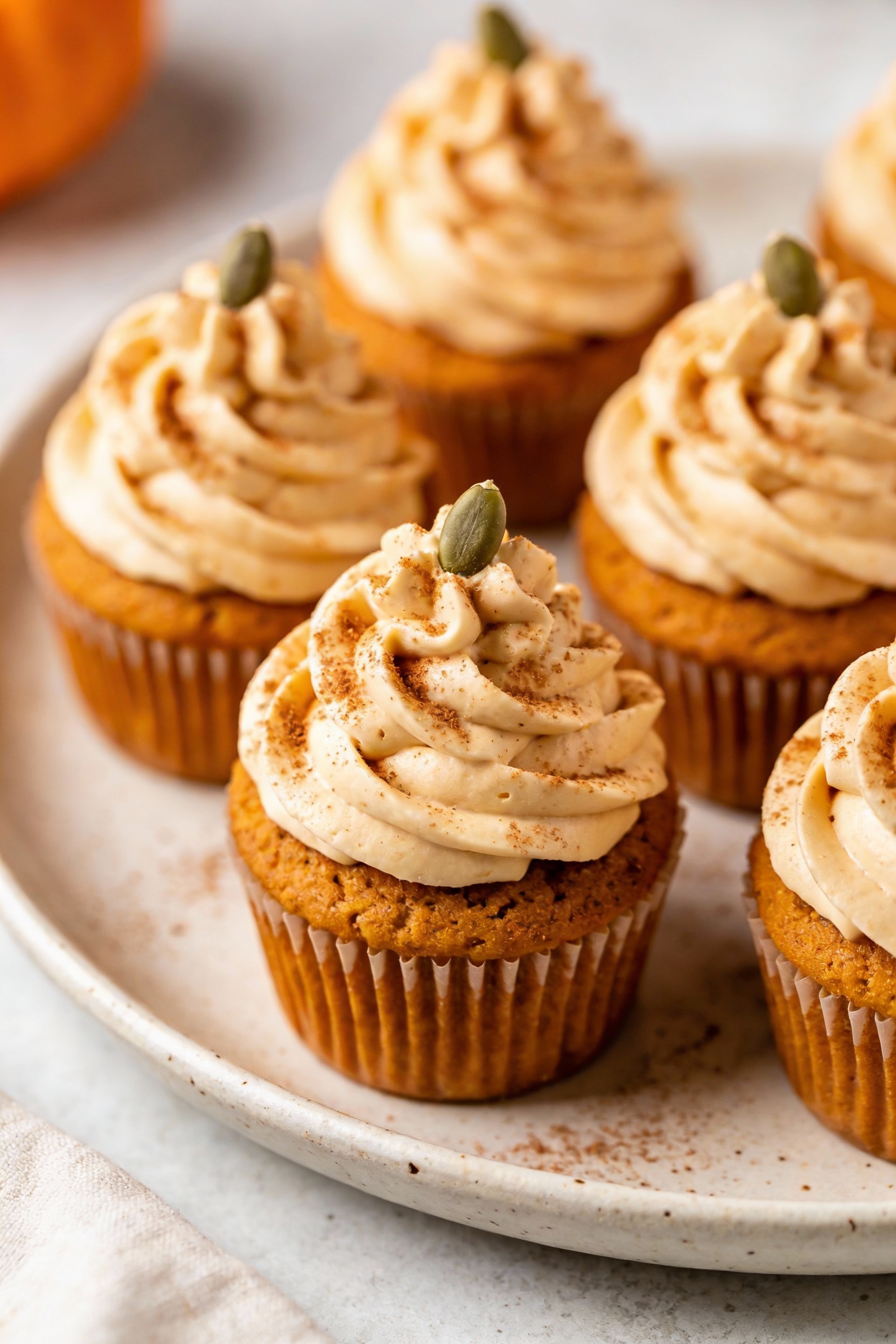 Final dish presentation: Pumpkin cupcakes with tall cream cheese frosting swirls, each topped with a single pepita and c