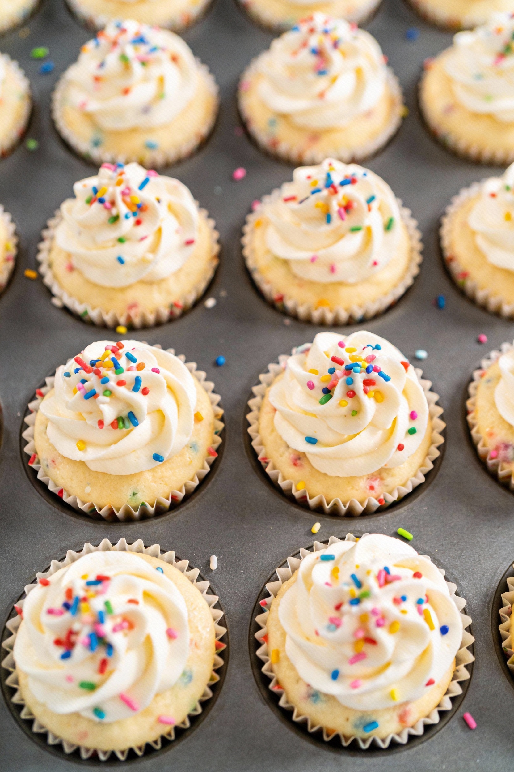 4. Top-down shot of funfetti cupcakes with evenly domed pale tops, generous vanilla buttercream swirls and rainbow sprin