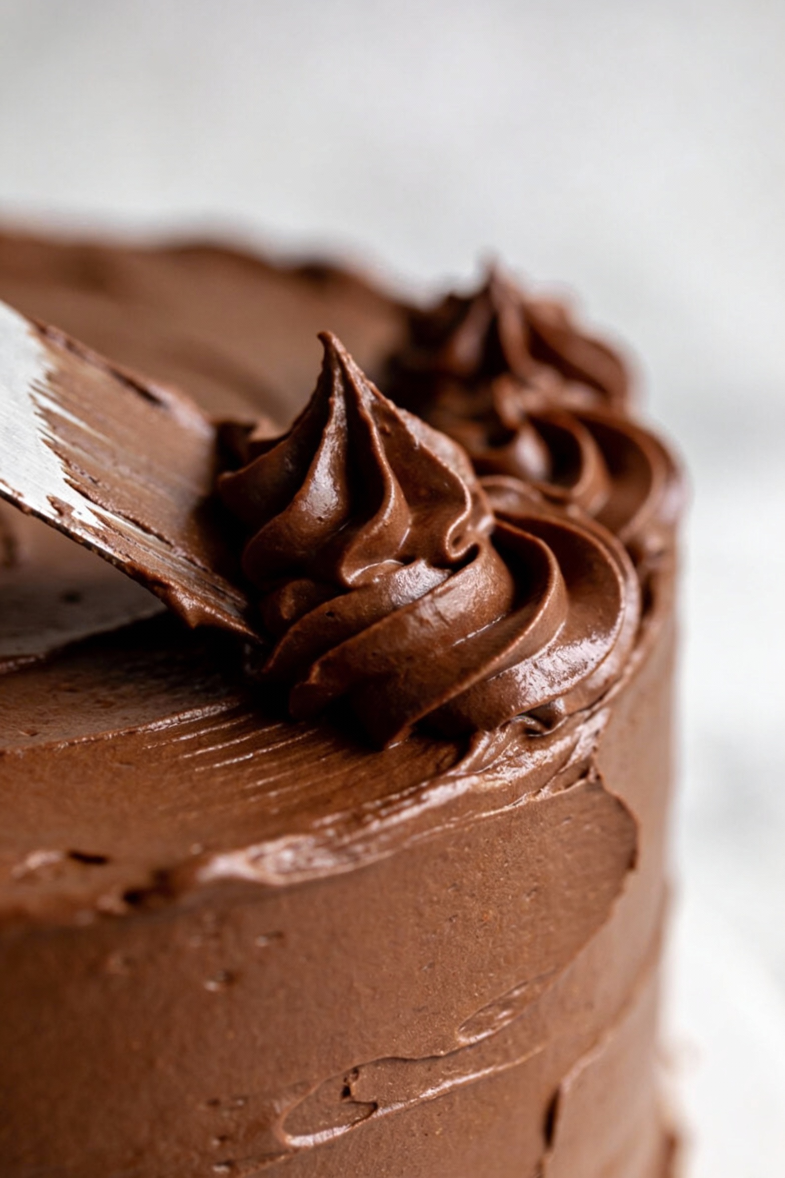 Close-up detail: thick chocolate buttercream being spread into smooth, swooping peaks on the cake side, visible spatula 